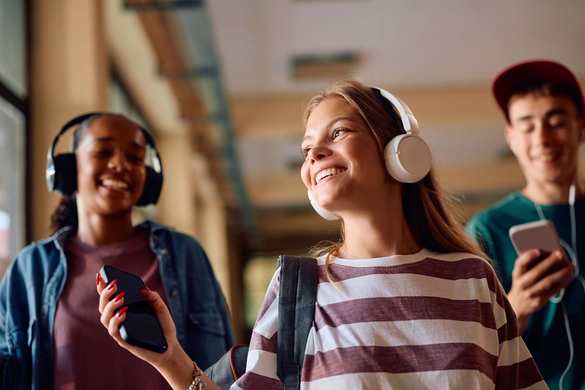 Happy teenager girl and her classmates listening music on headphones at high school.